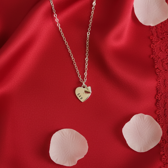 Valentine day Silver necklace with a heart-shaped pendant on a red fabric background with pink petals.